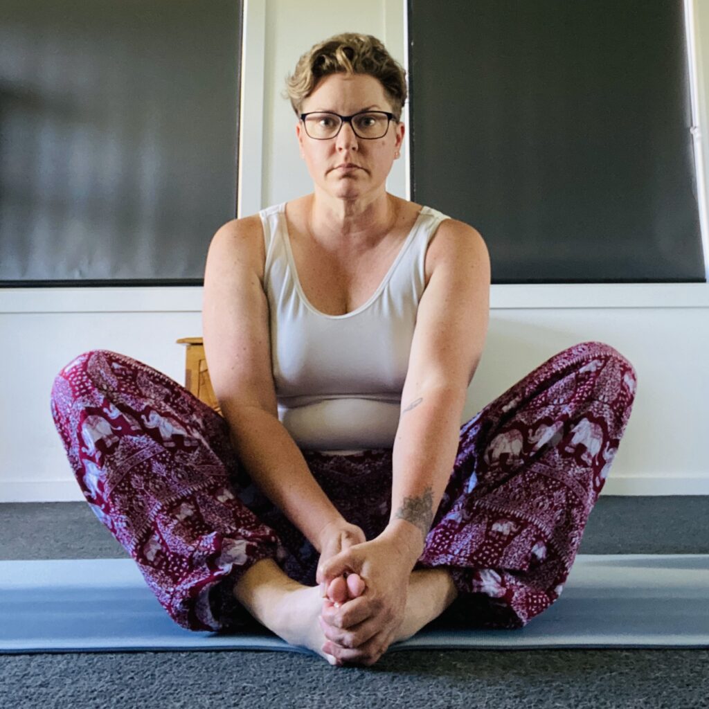 Em sitting in Butterfly pose - with the soles of her feed together and her knees splayed open. She looks (and feels) like her knees are up around her ears. She looks unhappy. She is.