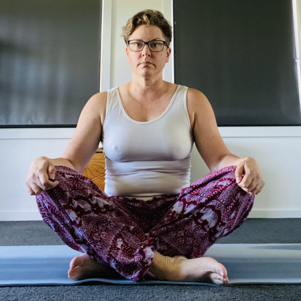 Em sitting cross-legged on the floor. Looking unhappy. Knees around her ears. Bitchy resting face game is strong.