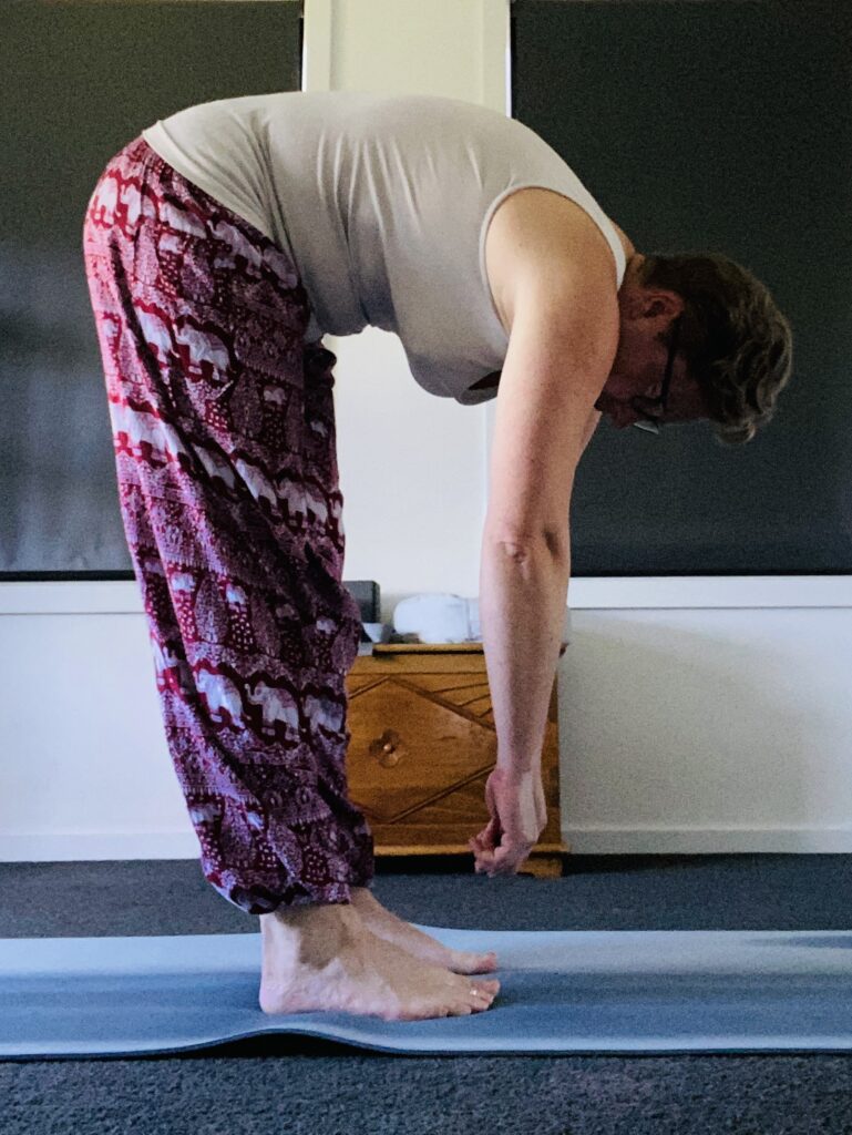 Em stands in a forward bend position.Her hands hang well short of the floor.