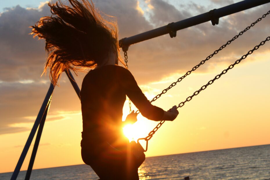 Silhouetted woman on a swing with the ocean and orange sunset in the background