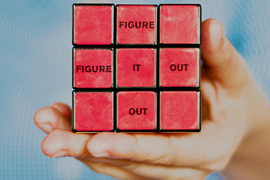 A hand holding a Rubiks cube with the words Figure It Out written on the side.