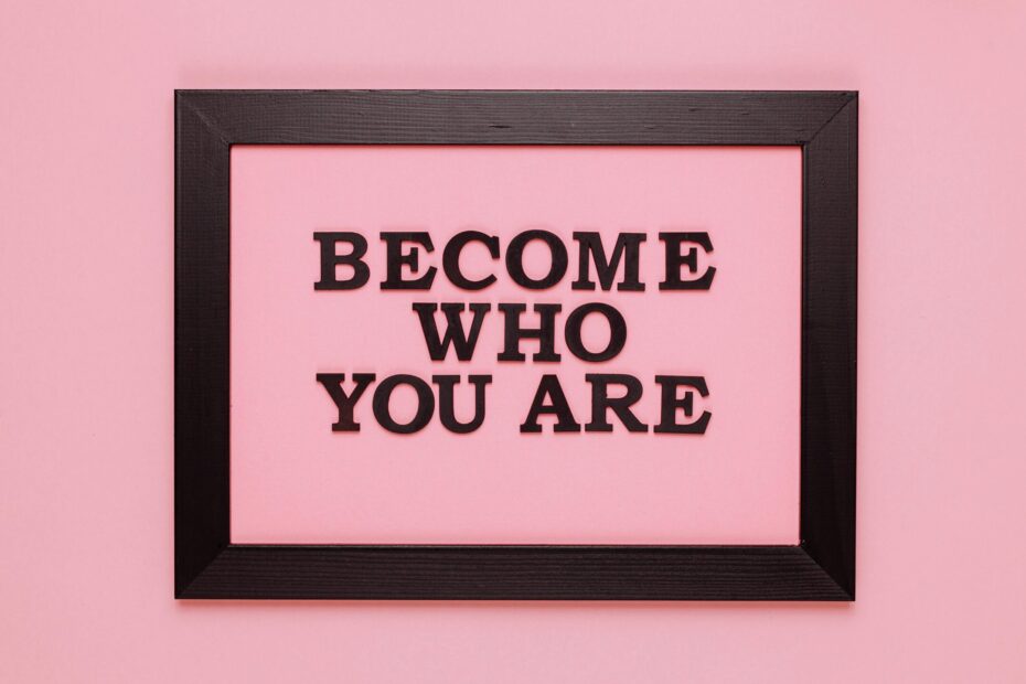 A black frame in front of a pink background. Inside the frame are the words "Become who you are."