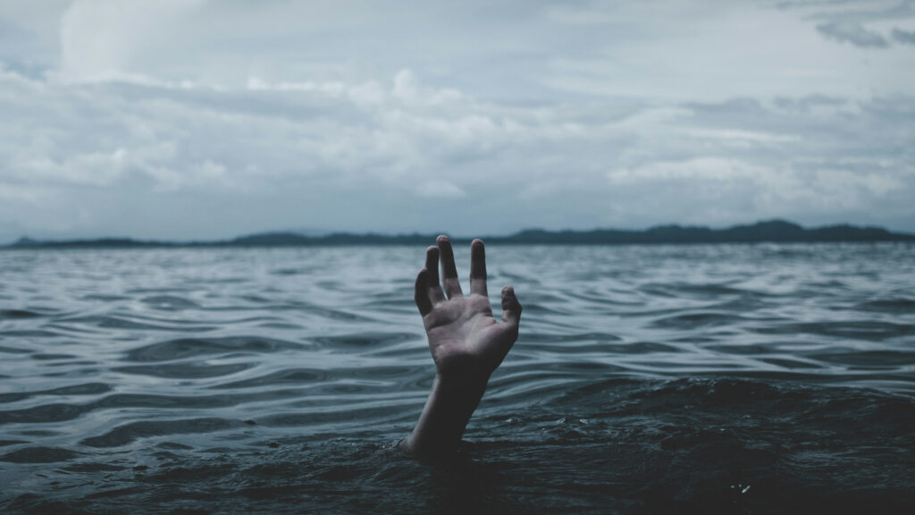 A hand reaches out from the sea, symbolising drowning. Being chronically overstimulated can make you feel like you’re drowning … in noise.